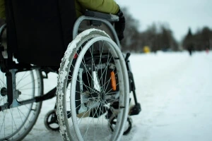 Low close-up image of the back of a man sitting in a wheelchair on heavy, snow-covered grounds